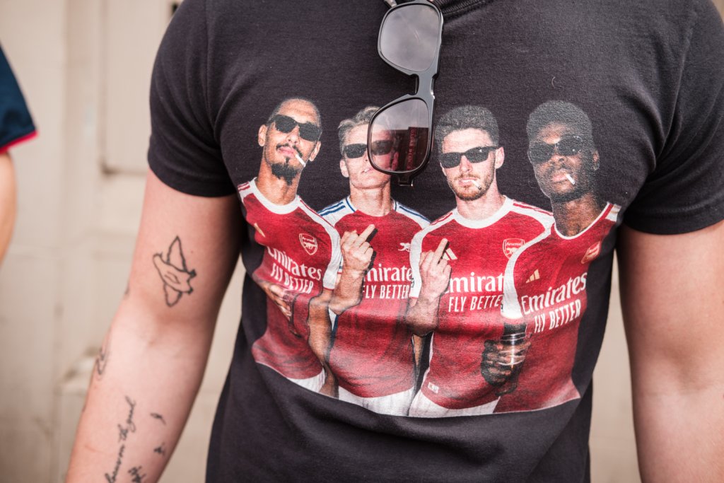A man is wearing a black t-shirt with four footballers each wearing sunglasses and Emirates football shirts.