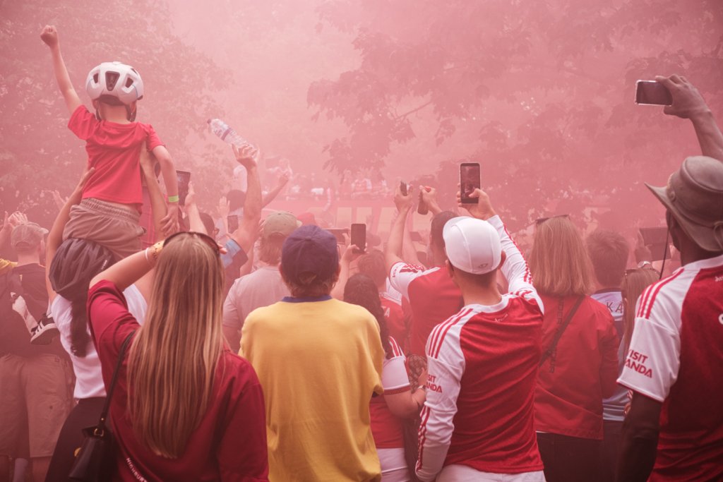 A group of Arsenal football supporters look on through a haze of red smoke as the team bus approaches.